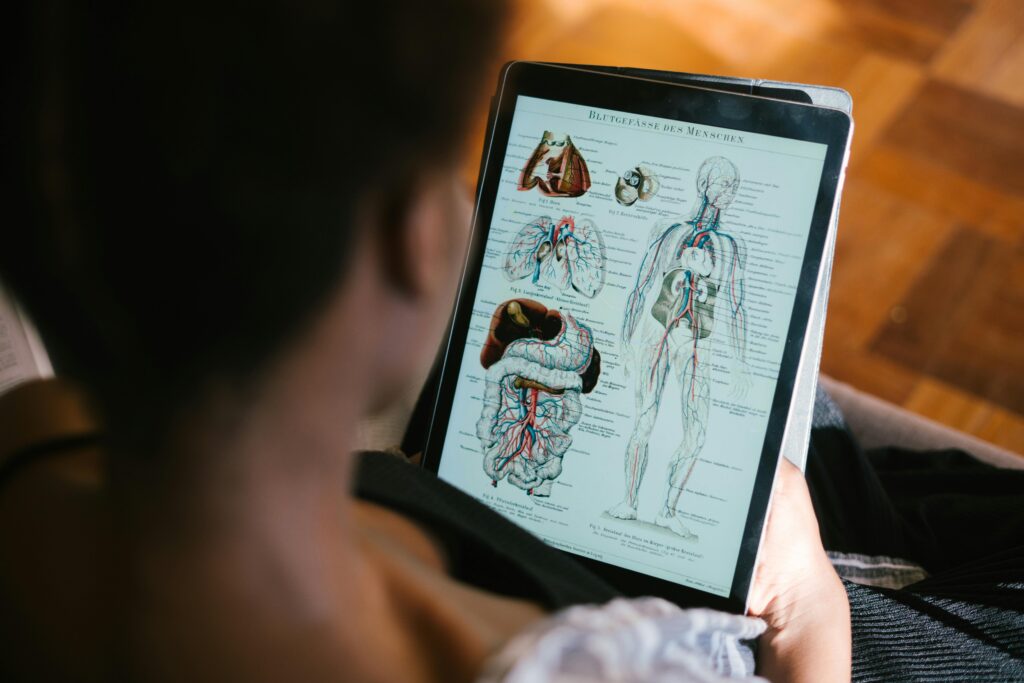 A woman studies anatomy diagrams on a tablet indoors, focusing on educational material.